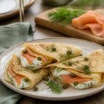 Crêpes au saumon fumé et Boursin roulées sur une assiette en ardoise, garnies d'aneth frais et de tranches de citron
