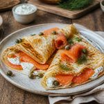 Crêpes au saumon fumé et crème fraîche roulées, garnies d'aneth frais et de tranches de citron, servies sur une assiette en céramique blanche