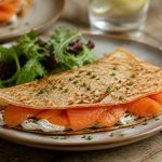 Crêpes au saumon fumé roulées, garnies de crème citronnée et d'aneth frais, servies sur une assiette en ardoise avec des tranches de citron
