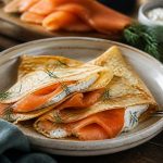 Crêpes au saumon fumé garnies de crème citronnée, d'aneth frais et de câpres, pliées en triangle sur une assiette blanche