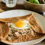 Crêpes salées au thon pliées en quatre, garnies d'une farce thon-fromage gratinée, servies chaudes sur une assiette blanche avec quelques brins de ciboulette