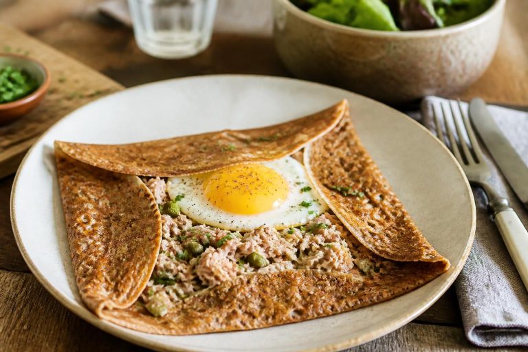 Crêpes salées au thon pliées en quatre, garnies d'une farce thon-fromage gratinée, servies chaudes sur une assiette blanche avec quelques brins de ciboulette