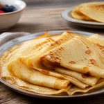 Assiette de crêpes sans lait dorées et moelleuses, garnies de confiture et de fruits frais, sur une table en bois clair