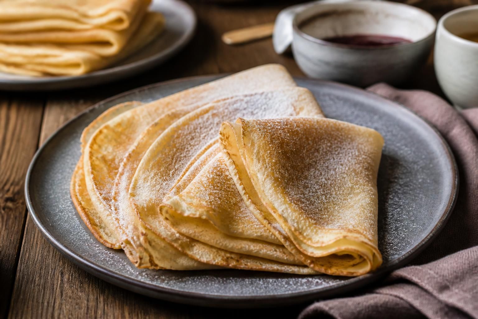 Assiette de crêpes sans lait dorées et moelleuses, garnies de confiture et de fruits frais, sur une table en bois claire