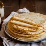 Assiette de crêpes sans lait dorées et fines, garnies de fruits frais et de sirop d'érable, sur une table en bois clair