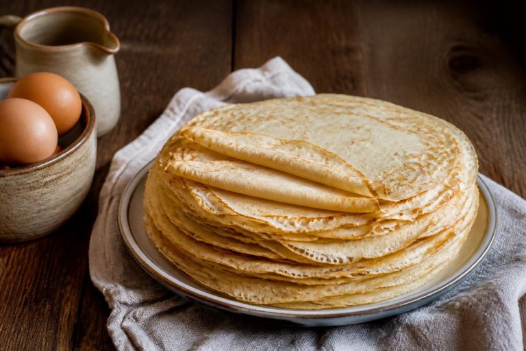 Assiette de crêpes sans lait dorées et fines, garnies de fruits frais et de sirop d'érable, sur une table en bois clair