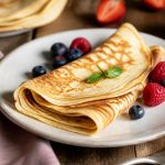 Pile de crêpes sans lait dorées et moelleuses, garnies d'un filet de miel et de tranches de banane, sur une assiette en céramique blanche
